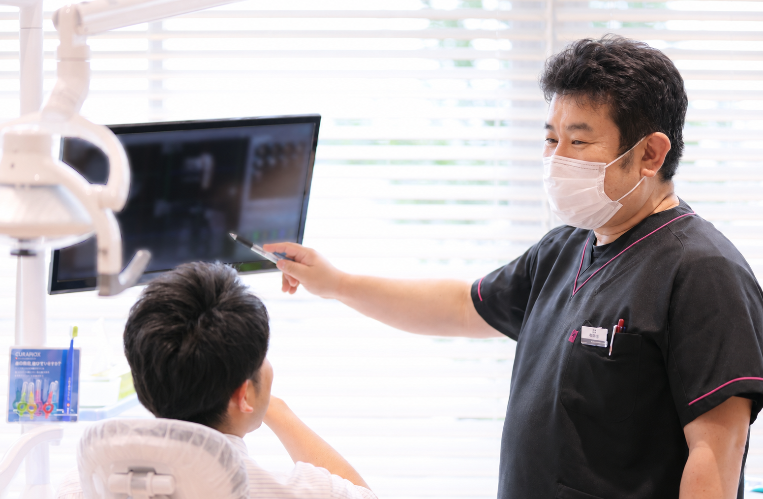 歯科医師がモニターに映した画像を指しながら、診療チェアの患者に説明している様子